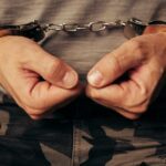 Handcuffed soldier in military army clothes. Prisoner of war or arrested terrorist, close up of hands in handcuffs, selective focus.